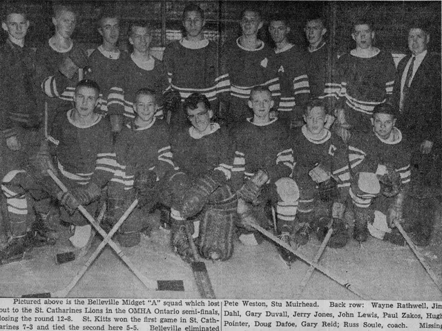The image shows a black and white photo of a hockey team, with some of them standing and some...