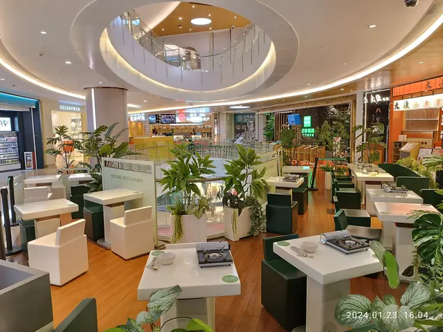 The image shows the interior of a restaurant with lots of tables and chairs, houseplants, plates,...