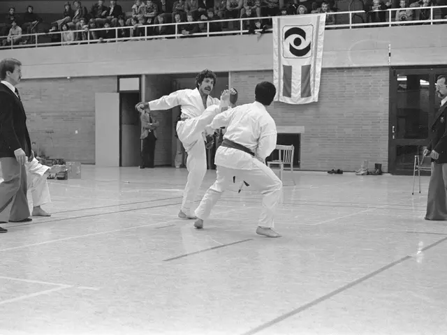 The image shows a group of people practicing karate in a gymnasium. There are men and women in the...