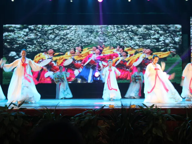 The image shows a group of people standing on top of a stage, illuminated by lights at the top and...