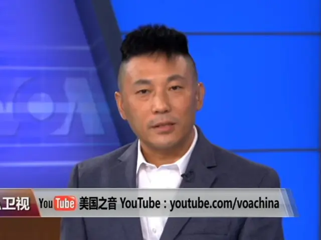 The image shows a man in a suit and tie on a TV screen, with text at the bottom of the image and a...