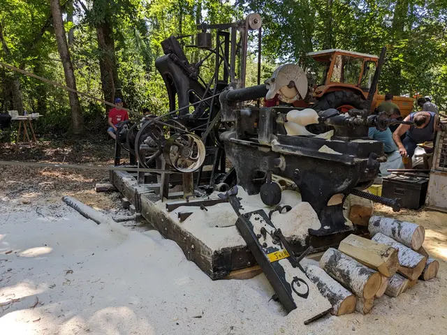 The image shows a group of people working on a machine in the woods. There are wooden logs, a...