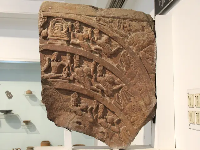 The image shows a large stone relief on display in a museum, with intricate carvings on its...