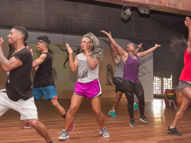 The image shows a group of people dancing in a dance studio, with a wall in the background...