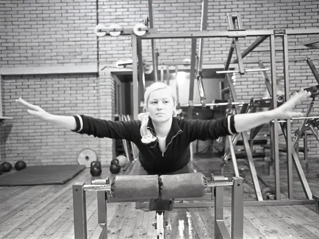 The image shows a woman doing pilates on a reformer in a gym, surrounded by gym equipment and balls...