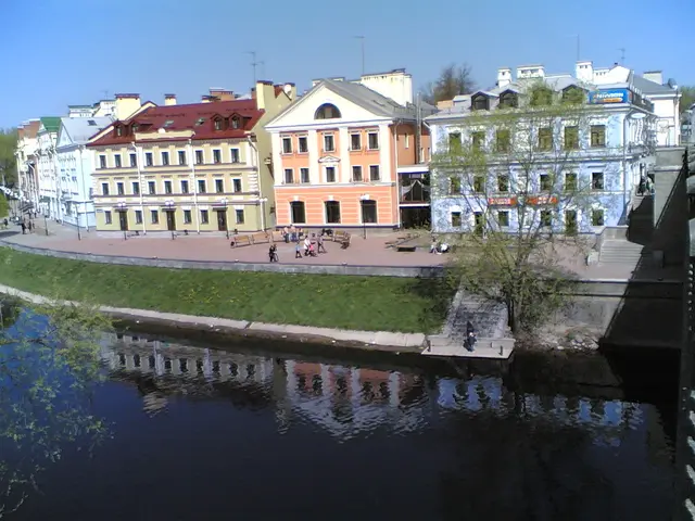 The image shows a river running through a city next to tall buildings, with a bridge on the right...
