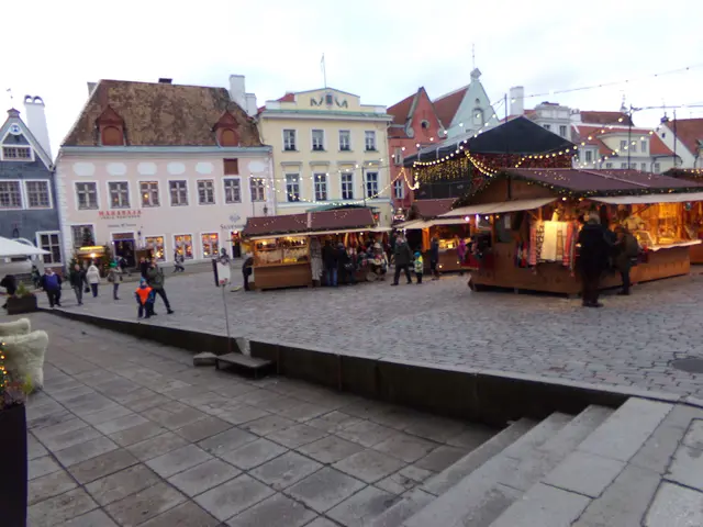The image shows a bustling Christmas market in Tallinn, Estonia. There are many people gathered...