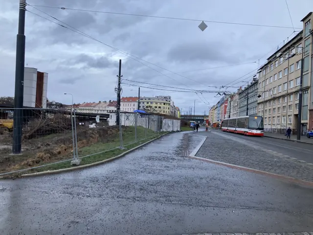 The image shows a city street with a bus driving down it, surrounded by buildings with windows,...