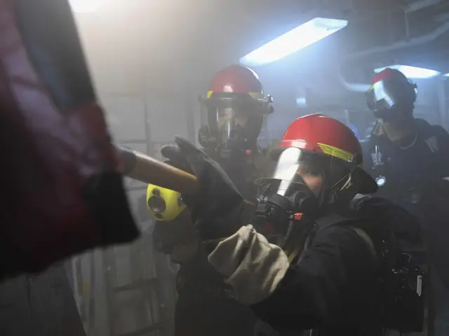 The image shows a group of people wearing gas masks and helmets, with one person holding an object...