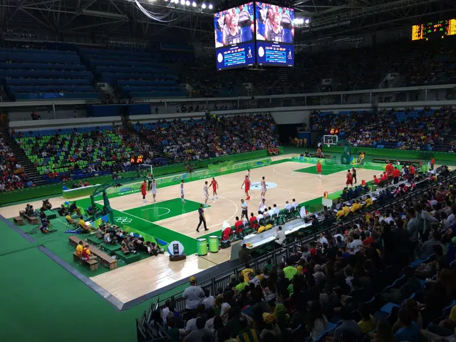 The image shows a large arena filled with lots of people watching a basketball game. There are...