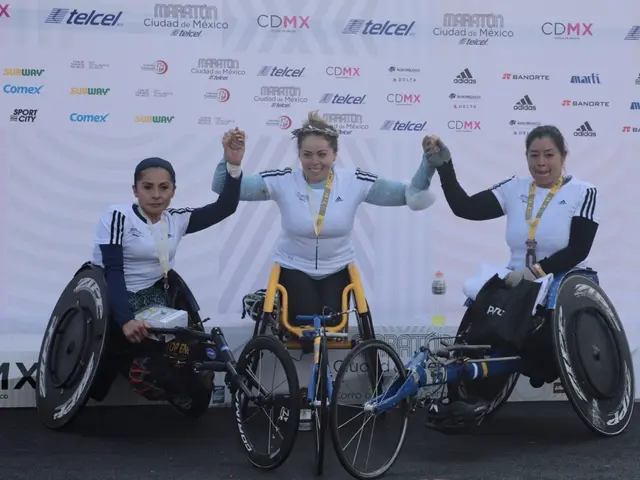 The image shows three women in wheelchairs standing on a podium with their hands in the air,...