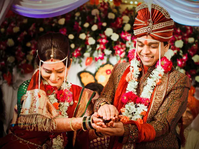 The image shows a man and woman dressed in traditional Indian attire, adorned with garlands,...
