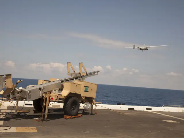 The image shows a military vehicle on the deck of an aircraft carrier, with a drone flying in the...
