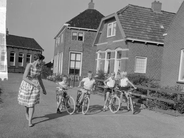 The image shows a group of children riding bicycles down a street, with a woman walking alongside...