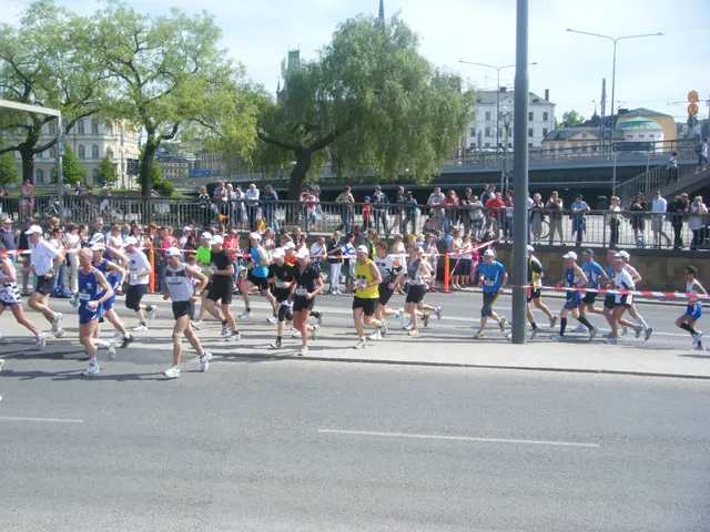The image shows a group of people running in a marathon on a road surrounded by a metal fence, a...