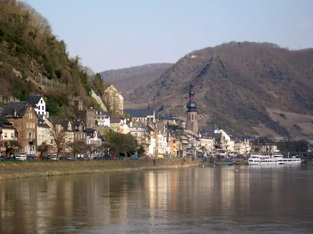 The image shows a picturesque view of a small town on the banks of a river, with boats on the...