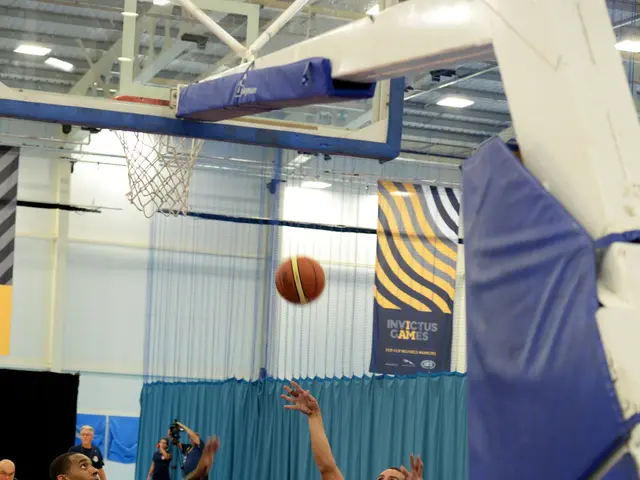 The image shows a group of people in wheelchairs playing basketball in a gymnasium. There is a...