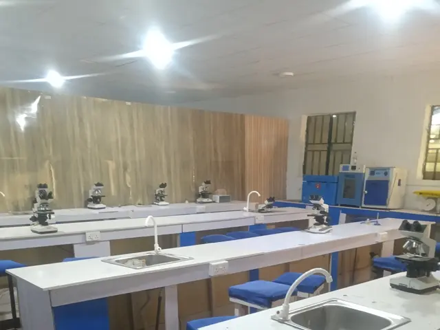 The image shows a laboratory with blue stools and white counter tops, a sink with taps, machines, a...