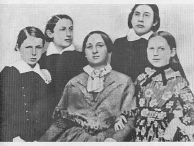 The image shows a black and white photo of a group of women, with one of them sitting in the...