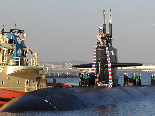 The image shows a group of people standing on top of a submarine in the water, with a boat in the...