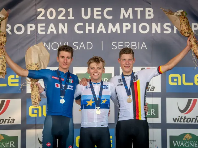The image shows three men standing on top of a podium, wearing medals and holding flower bouquets...