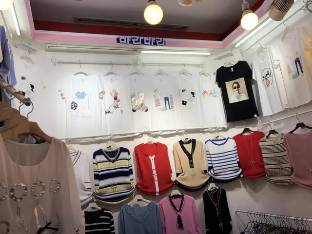 The image shows a clothing store with a variety of t-shirts hanging on a rack, illuminated by...