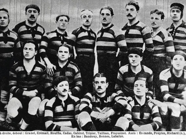 The image shows a black and white photo of a rugby team, with some standing and some sitting, in...