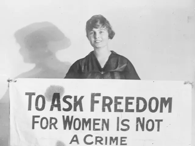 The image shows a woman standing and smiling while holding a banner that reads "To Ask Freedom for...