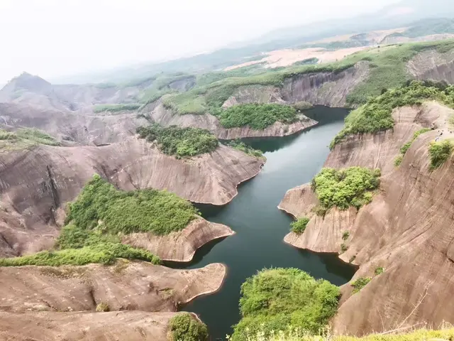 The image shows a stunning view of a large body of water surrounded by lush green hills and trees,...