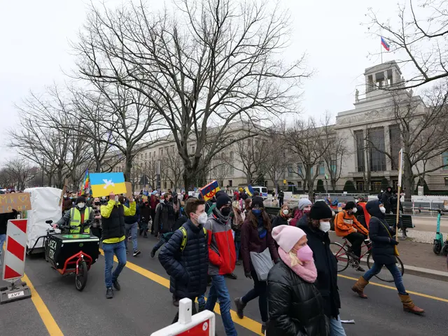 The image shows a large group of people walking down a street in front of a building, some of them...