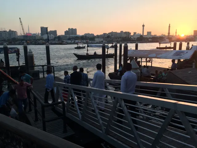 The image shows a group of people standing on top of a pier next to a body of water, with boats in...