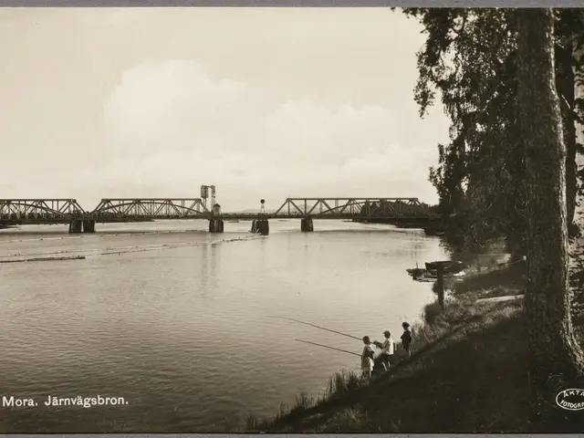 The image shows a black and white photo of people fishing on a river with a bridge in the...