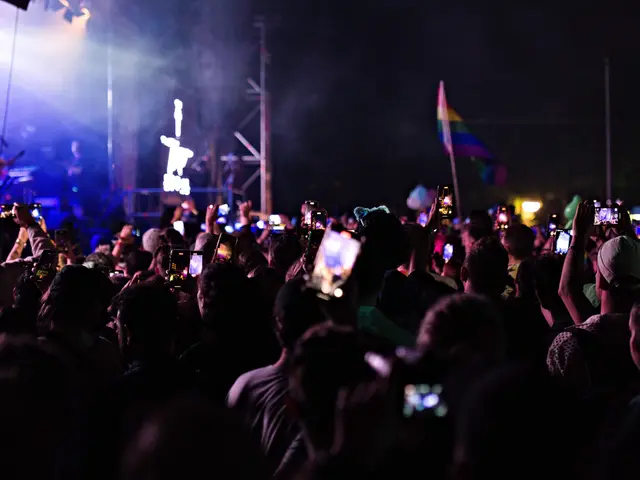 The image shows a crowd of people at a concert with their cell phones in the air, illuminated by...