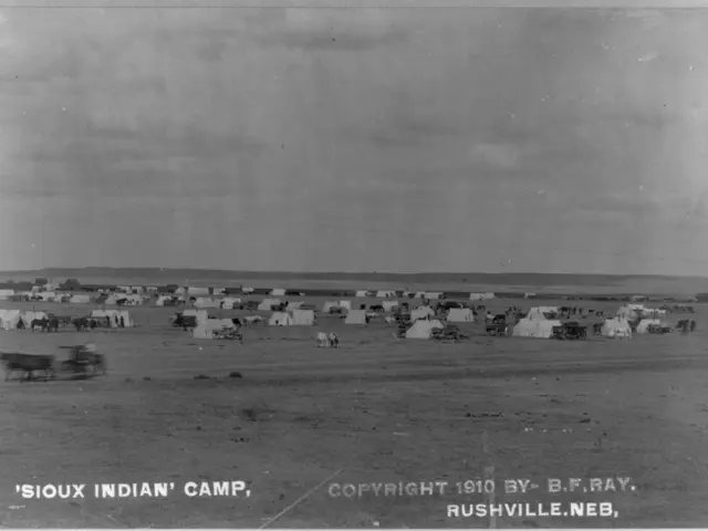 The image shows a black and white photo of a Sioux Indian camp in Rushville, Nebraska. There are...