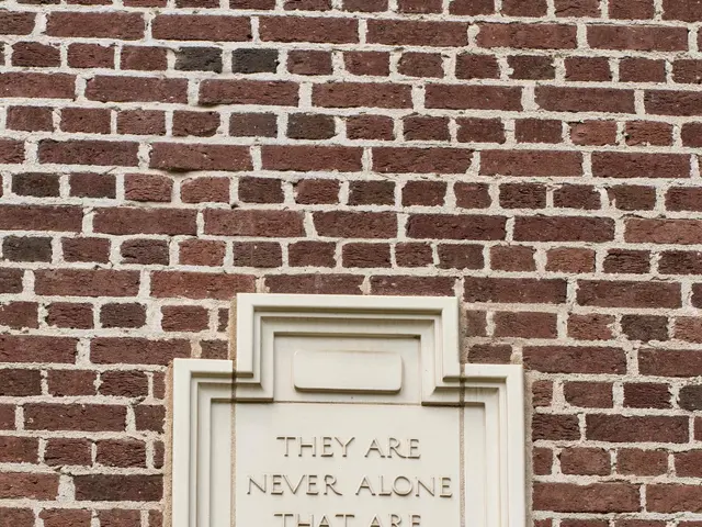 The image shows a brick wall with a plaque on it that reads "They are never alone that are...
