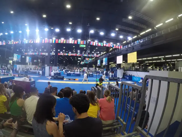 The image shows a large crowd of people sitting in front of a stage, with some standing on the...