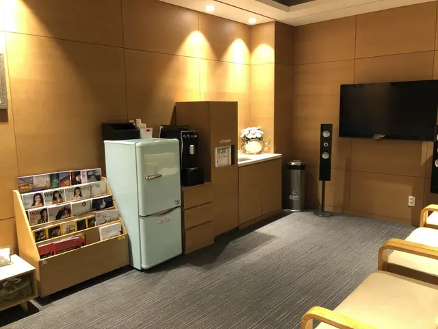 The image shows a living room with a sofa set, books arranged in the cupboards, a refrigerator, a...