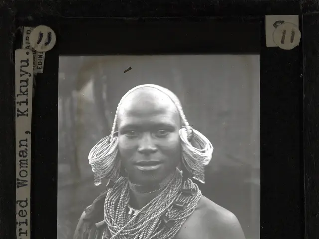 The image shows a black and white photo of a woman from the Kikuyu tribe wearing ornaments. The...