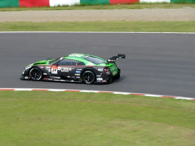 The image shows a sports car driving on a race track with grass on either side of the road and a...