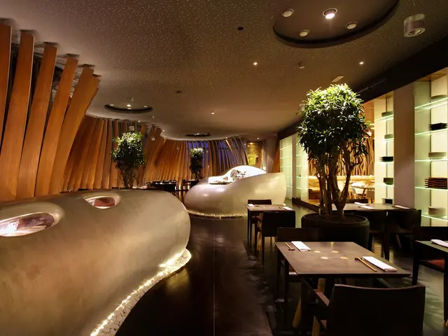 The image shows a restaurant with tables and chairs in front of a large window, surrounded by...