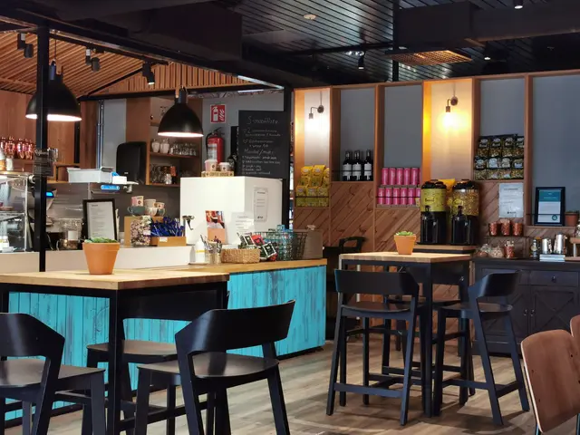 The image shows the interior of a restaurant with wooden tables and chairs, a flower pot with a...