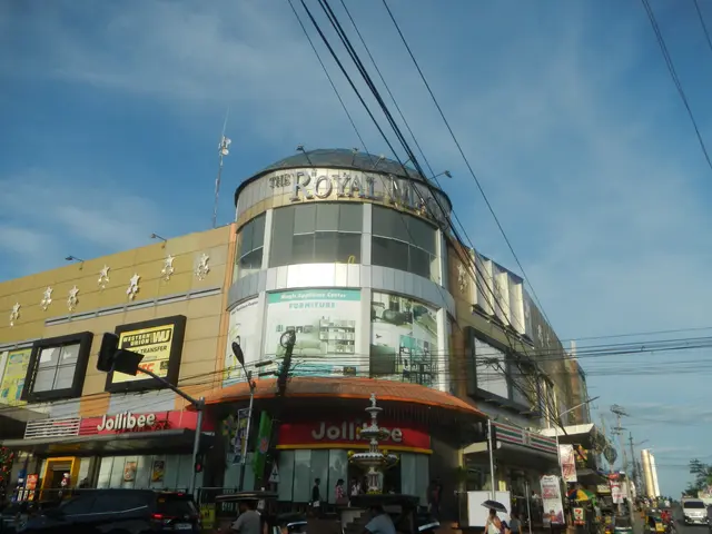 The image shows a bustling city street with vehicles driving on the road, people walking on the...