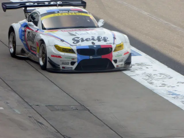 The image shows a BMW Z4 GT3 race car driving on a race track. The car is painted in a bright blue...