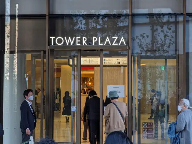 The image shows a group of people standing in front of a building with glass walls and doors. Some...