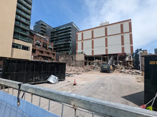 The image shows a construction site with a large building in the middle of it, surrounded by a...