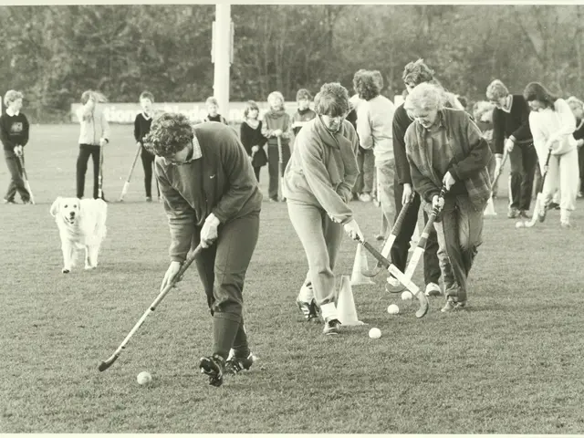 The image shows a group of people playing field hockey on a grassy field, with a dog accompanying...
