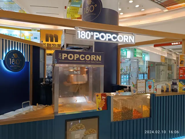 The image shows a popcorn stand in the middle of a shopping mall, with a countertop filled with...