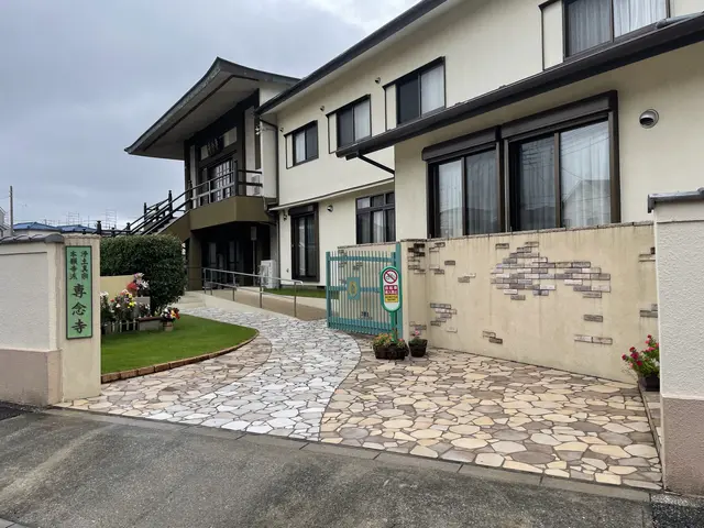 The image shows the entrance to a building with a stone walkway leading up to it, surrounded by...