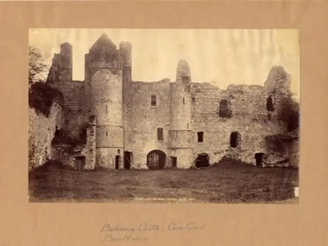 The image shows an old black and white photo of a castle in the middle of a field, surrounded by...