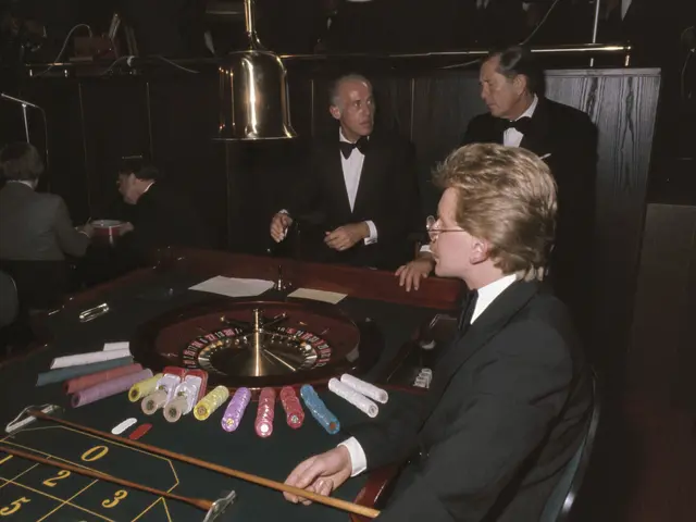 The image shows a man in a tuxedo playing roulette at a casino. He is sitting in a chair at the...